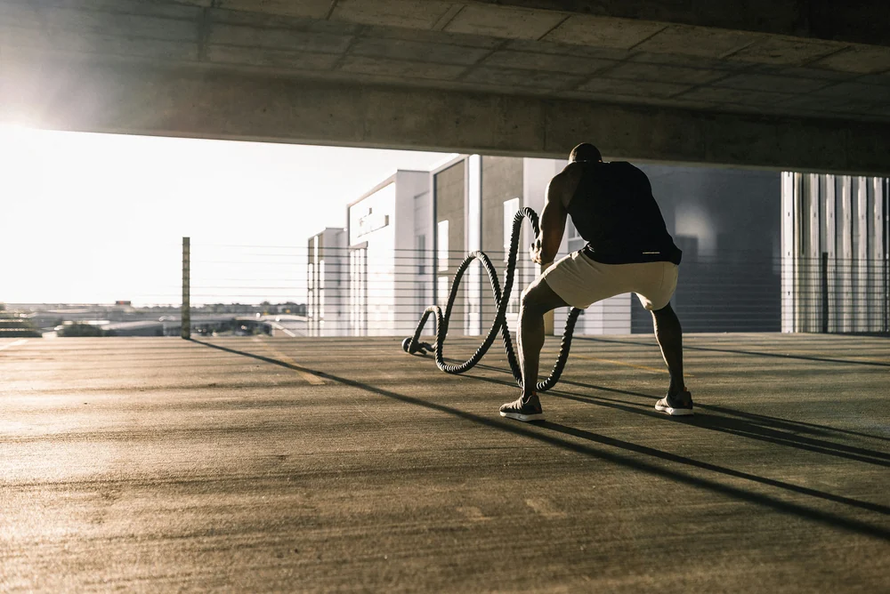 Man training with battle ropes in a sunlit parking garage